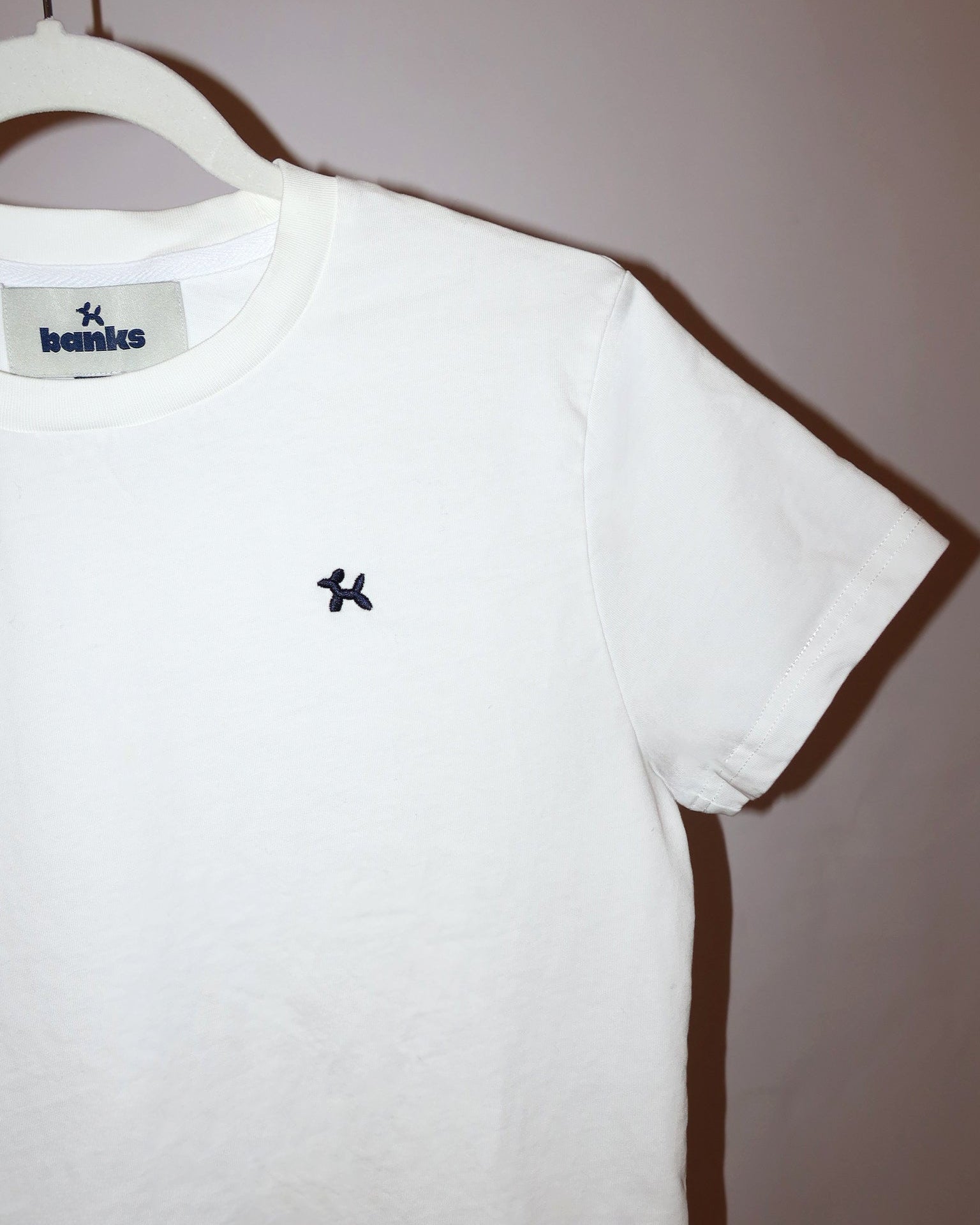 White t-shirt with a logo on a hanger against a plain background
